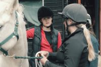 A woman veterinarian or instructor stands next to a younger female veterinary graduate; both are beside a grey horse.