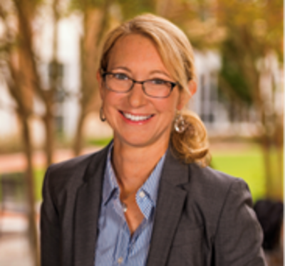 A woman wearing glasses and a blazer smiling at the camera