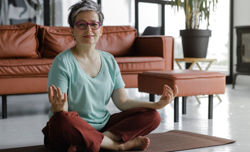A middle-aged woman with short, grey hair and glasses practicing yoga at home. 
