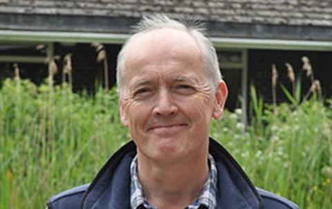 Mark Castle pictured outside, standing in front of some green foliage 