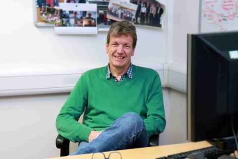 Professor James Wood sat at desk in an office wearing a green jumper