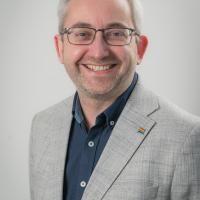 Head and shoulders image of Matthew Redford wearing a grey suit and smiling at the camera