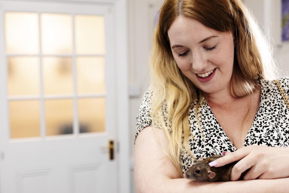 A smiling woman stroking a rat