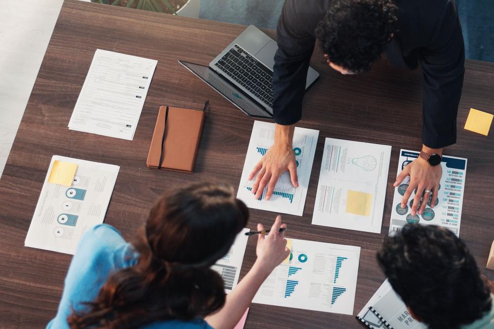 Three people looking at papers on a desk. 