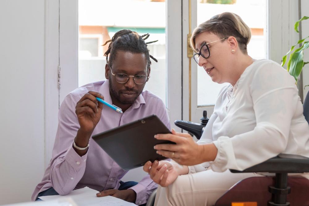 A woman using a wheelchair and a man review information on a screen together.
