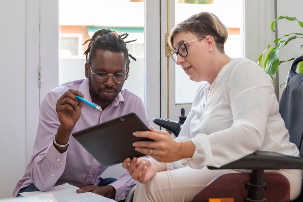 A woman using a wheelchair and a man review information on a screen together.