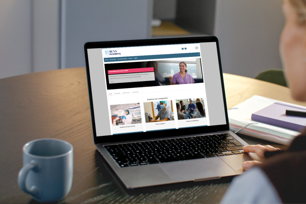 Person sits at a table looking at the Academy page on a laptop