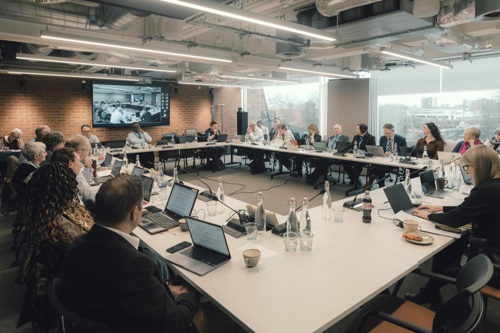 Photograph shows a group of professionals seated around a conference table during a meeting. 